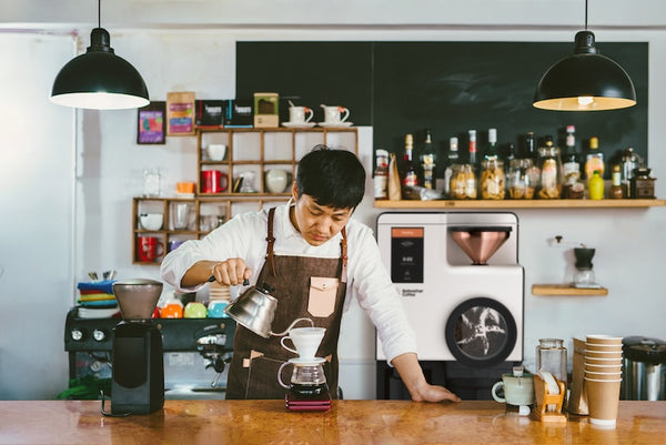 Person pouring coffee in a cafe with a Bellwether roaster behind them